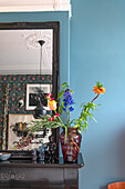 Colorful flower arrangement in a red glass vase on a black mantelpiece against a blue-painted wall