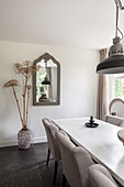 Dining area with white table, upholstered chairs, mirror and pendant light