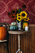 Herbstlicher Blumenstrauß aus Sonnenblumen (Helianthus) und Kürbisse auf rundem Tisch