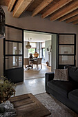 Wohnzimmer mit Holzbalkendecke und schwarzer Glastür zum Essbereich