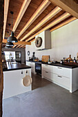 Modern kitchen with concrete floor, white cabinets and wooden beamed ceiling