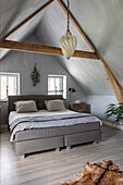 Double bed under sloping ceiling in concrete look with exposed wooden beams