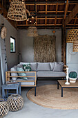 Lounge corner with light grey sofa and rattan lamps under a wooden beamed ceiling