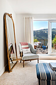 Armchair and large standing mirror in bright room with balcony access