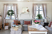Bright country-style living room with white wooden walls, grey sofa and lots of cushions