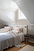 Sloping ceiling room with bed, patterned stool and natural light