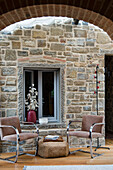 Two chairs and wicker stools in front of a rustic stone wall in the living room