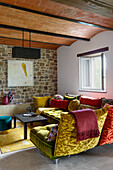 Living room with colorful velvet-covered sofa, stone wall and vaulted ceiling