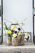 Daffodils, tulips and birch twigs in jars wrapped in sackcloth