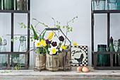Narzissen, Tulpen und Birkenzweig in Gläsern mit Sackstoff umwickelt und Hühnereier auf Stroh