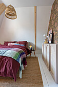 Bedroom with rattan lamp, patterned wallpaper and sisal carpet