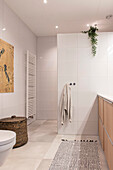 Modern bathroom with white tiled walls, light-colored wooden cabinet and woven laundry basket