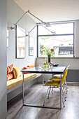 Dining area with yellow chairs and bench in bright room with large window