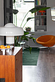 Modern living room with wooden chest of drawers, designer lamps and orange armchair