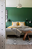 Bedroom with green-painted wall, double bed and modern wooden stool