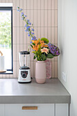 Bouquet of flowers in pink vase on kitchen counter next to blender