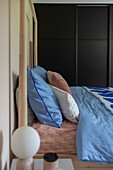 Wooden bed with blue bed linen, salmon-colored fitted sheet and accent pillows in the bedroom