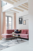 Living room with pink corner sofa, white-painted ceiling beams and pictures