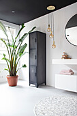 Modern bathroom with locker, round mirror and large plant