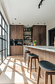 Kitchen with dark wooden cupboards, island and bar stools in front of floor-to-ceiling windows