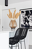 Black rattan chairs at a white kitchen island with dried flower arrangement