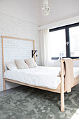 Bright bedroom with light-colored wooden bed in front of a white brick wall