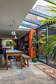 Dining area with glass roof, long wooden table, colorful chairs and bench seat