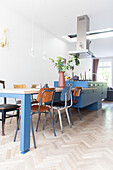 Open-plan kitchen with blue cooking island, extractor hood, dining table and chairs