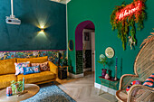 Living area with yellow velvet sofa, green wall and neon lettering