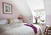 Dachgeschoss-Schlafzimmer im Landhausstil mit Blumenbettwäsche und Orchideen am Fenster