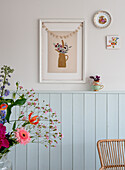 Floral picture and garland over pastel-colored wood paneling in the living room