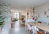 Open-plan living dining area with floral wallpaper and light-colored wooden furniture