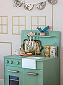 Children's play kitchen in pastel green with toy crockery and decorative tins