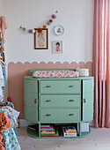 Mint-colored changing unit with flower changing mat and wall decoration in the nursery