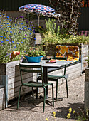 Small seating area with metal chairs and flowering raised bed in the garden