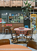 Table with checkered tablecloth and wooden chairs, sales counter, drinks and wooden crates