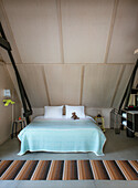 Double bed with turquoise bedspread and striped carpet in bedroom under sloping ceiling