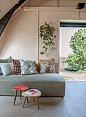 Modern living room with grey sofa and vintage stools, open door to the garden