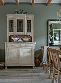 Country-style kitchen hutch next to wooden chairs and large mirror