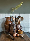 Rustic kitchen scene with ceramic jugs, wooden spoons and eggs on a wooden board