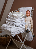 White pile of linens and vintage doll on wooden chair