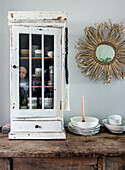 Vintage kitchen cupboard with crockery next to rustic mirror and candle