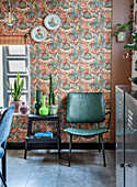 Green chair, stool and plants in front of retro-style patterned wallpaper