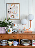 Cupboard with crockery, lamp and houseplant, picture on the wall