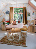 Room with dining table in pink, white chairs with seat cushions, vintage carpet and walls with dot pattern