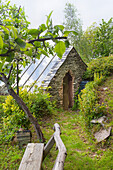 Stone garden shed with glass roof next to fruit tree and wooden bench in the garden