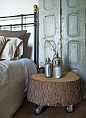 DIY bedside table made from tree stump with metal bottles and lamp in vintage bedroom