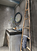 Rustic bathroom with concrete walls, ladder towel rail and round mirror