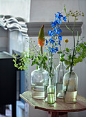 Various wildflowers in glass bottles on a small wooden table