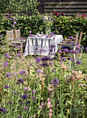 Flower garden with laid table and wooden furniture in the summer